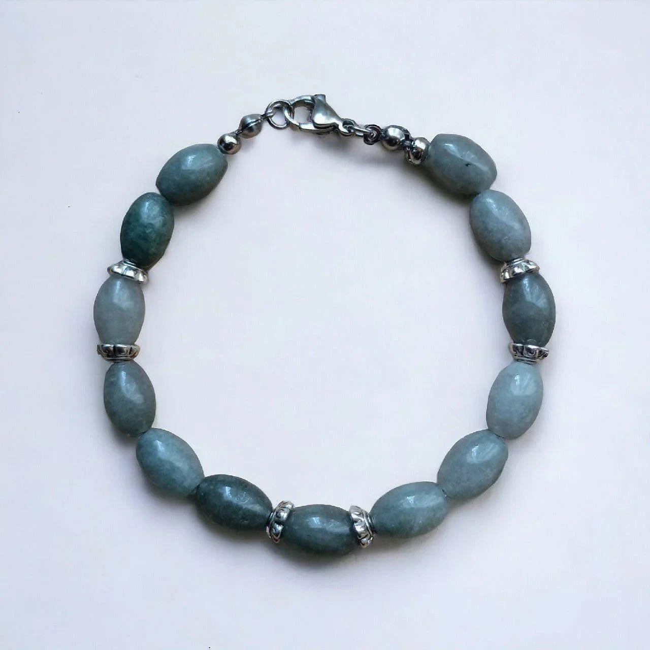 Bransoletka handmade z zielonych kamieni naturalnych i srebrnych elementów na białym tle