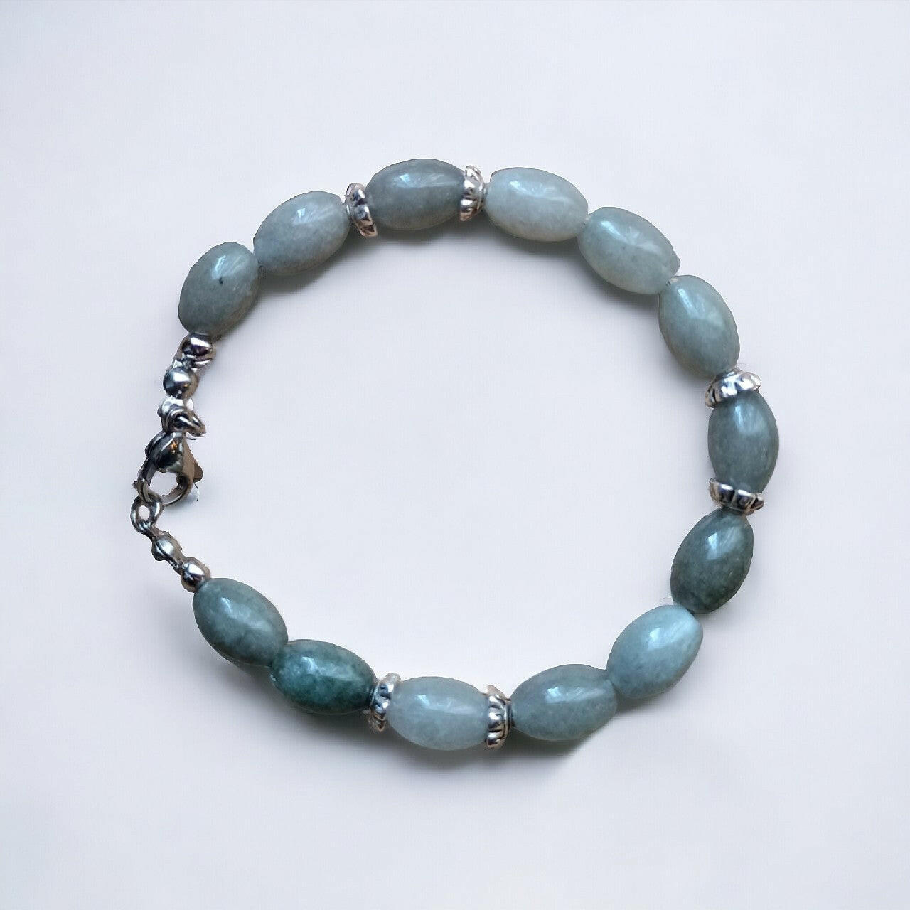Elegancka bransoletka handmade z polerowanych jadeitów o subtelnej, szaro-zielonej barwie. Urozmaicona metalowymi elementami o ciekawej fakturze. Wyposażona w solidne, metalowe zapięcie.