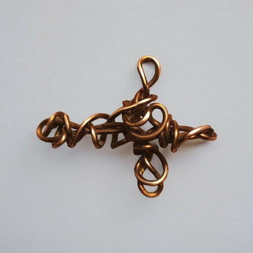 Ręcznie formowany wisiorek w kształcie krzyża z czystej miedzi, z ozdobnymi detalami uzyskanymi dzięki technice wire wrapping. Długość 6 cm.