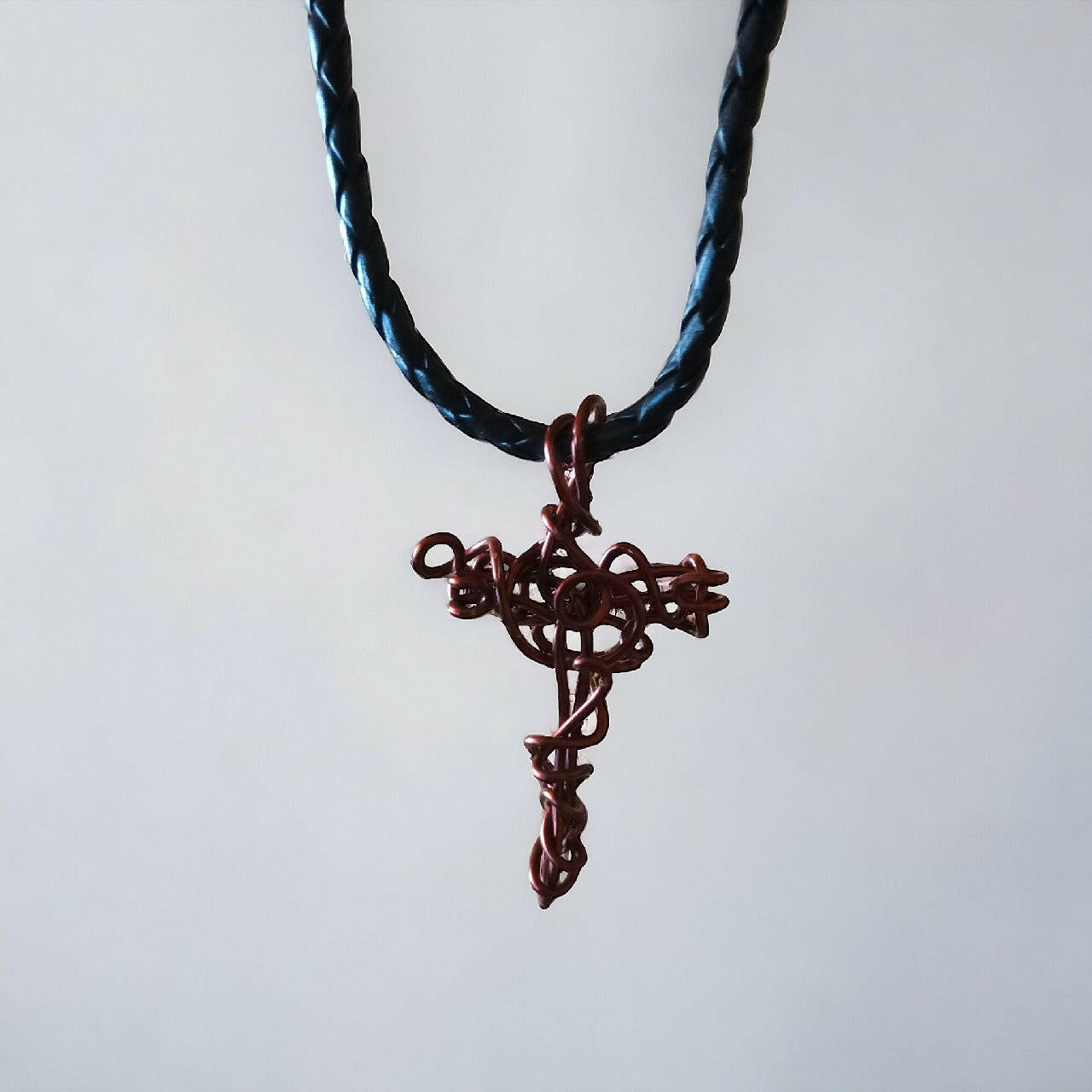 Miedziany wisiorek w kształcie krzyżyka, wykonany z czystej miedzi techniką wire wrapping. Zawieszony na czarnym, plecionym rzemieniu z solidnym zapięciem.