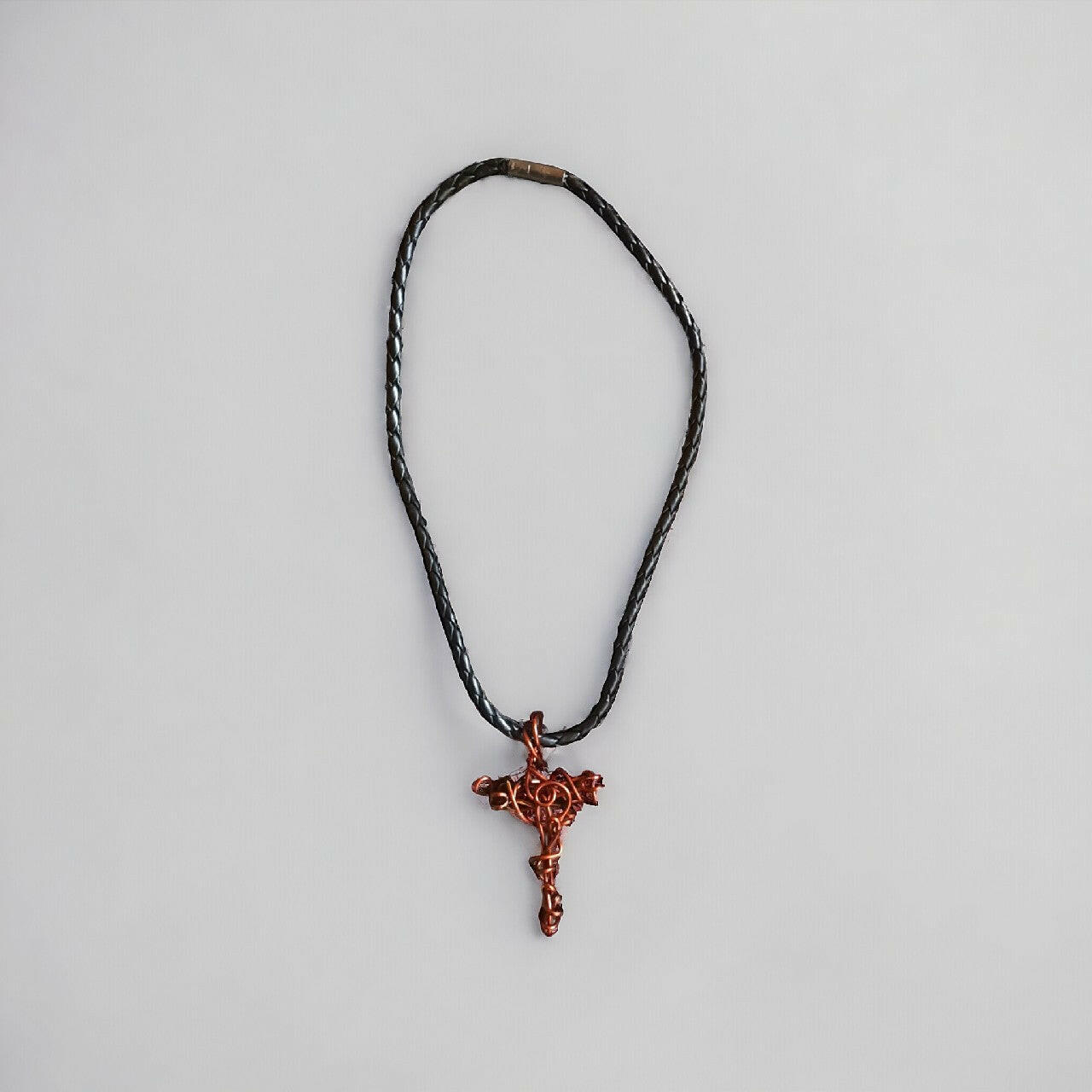 Wisiorek handmade w kształcie krzyża, wykonany z czystego miedzianego drutu techniką wire wrapping. Miedz ma ciepły, naturalny odcień. Zawieszony na solidnym, czarnym, plecionym rzemieniu z bezpiecznym zapięciem.