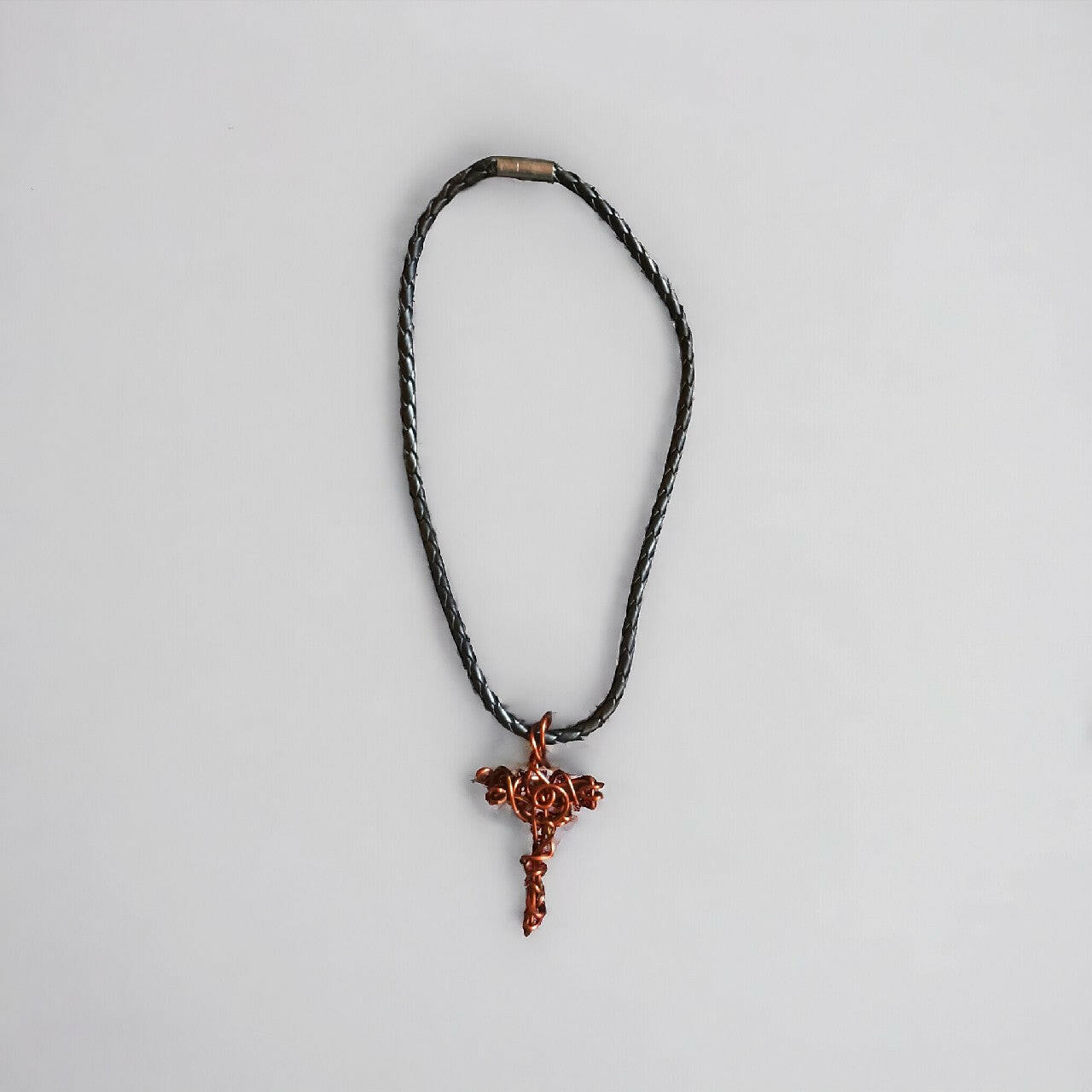 Prosty, a zarazem wyrazisty wisiorek w formie krzyżyka z czystej miedzi, z charakterystycznym oplotem wire wrapping. Zawieszony na wytrzymałym, plecionym rzemieniu w kolorze czarnym z mocnym zapięciem.