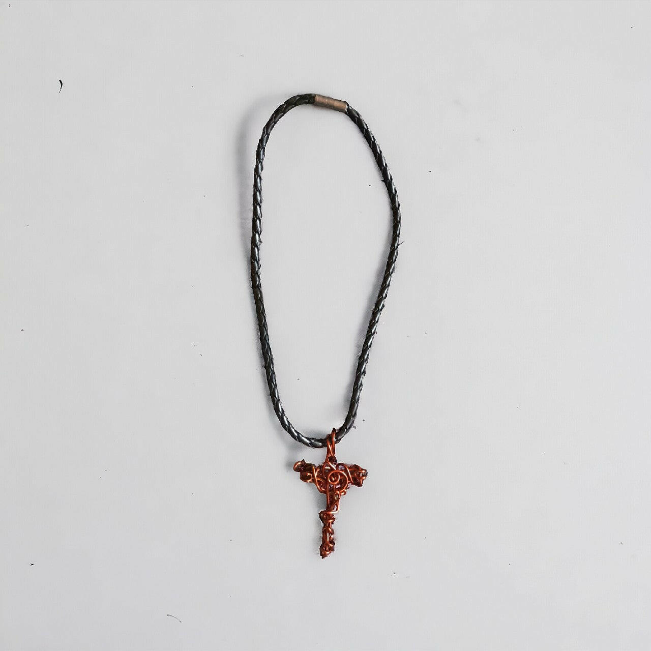 Wisiorek z czystej miedzi, ręcznie formowany w kształt krzyżyka techniką wire wrapping. Miedz nadaje mu rustykalny charakter. Zawieszony na solidnym, czarnym, plecionym rzemieniu z pewnym zapięciem.