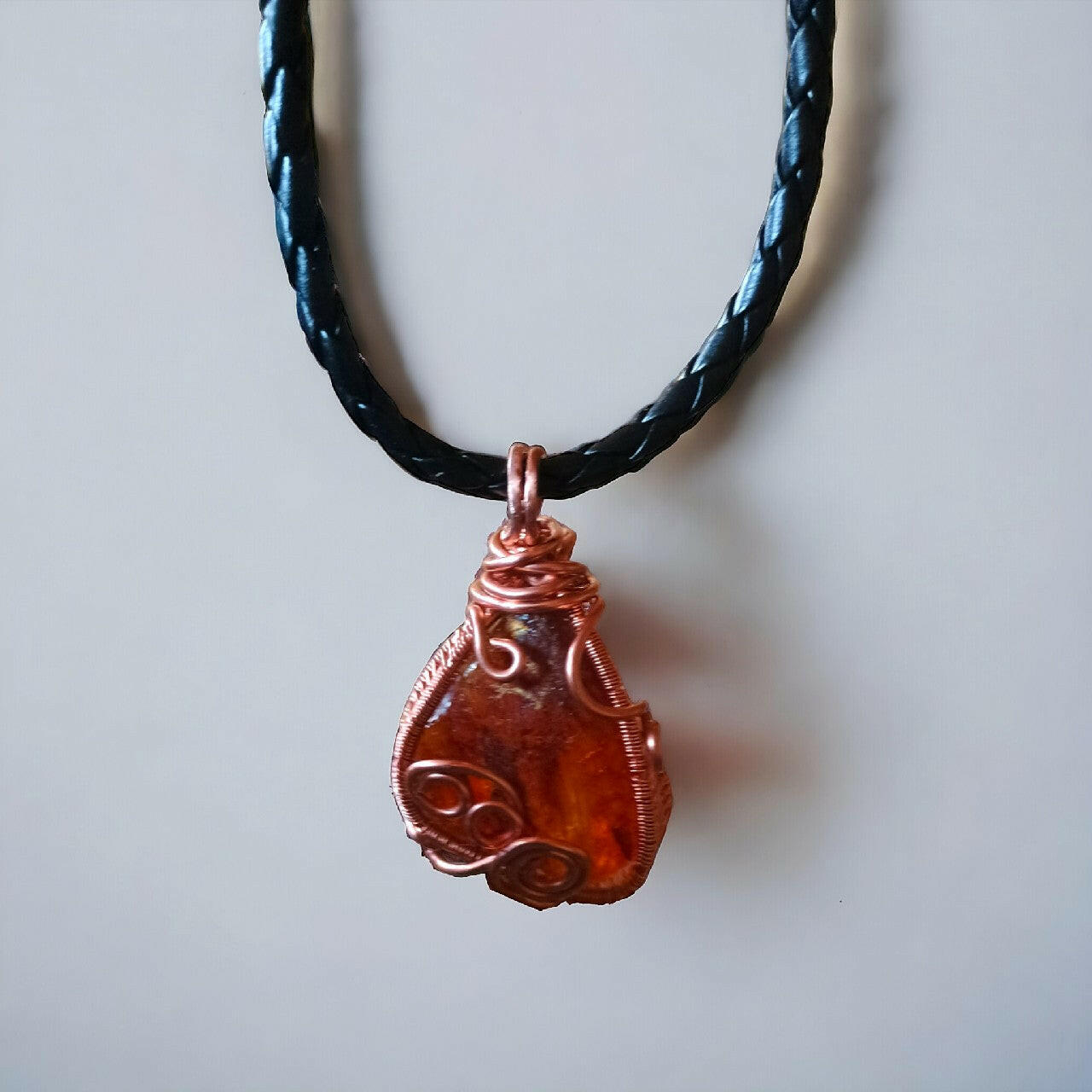 Wisiorek z surowej, nieregularnej bryłki bursztynu bałtyckiego, ozdobnie oplecionej miedzianym drutem techniką wire wrapping. Zawieszony na czarnym, plecionym rzemieniu z mocnym zapięciem magnetycznym. Długość naszyjnika wynosi 42 cm.