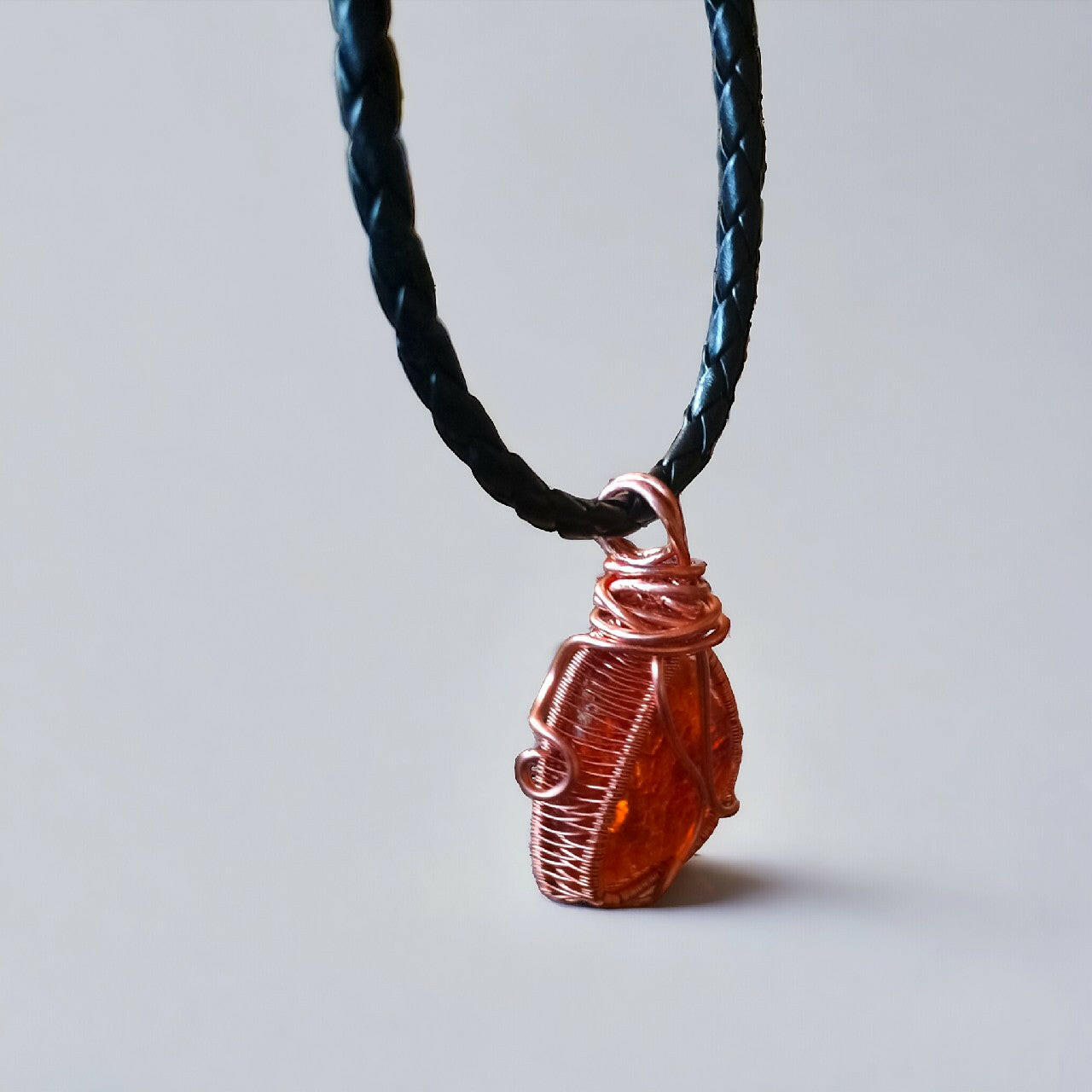 Ręcznie wykonany wisiorek przedstawiający naturalną bryłkę bursztynu bałtyckiego w miedzianej oprawie wire wrapping. Bursztyn o ciepłej, miodowej barwie. Zawieszony na eleganckim, plecionym rzemieniu w kolorze czarnym, z praktycznym zapięciem magnetycznym. Długość 42 cm.