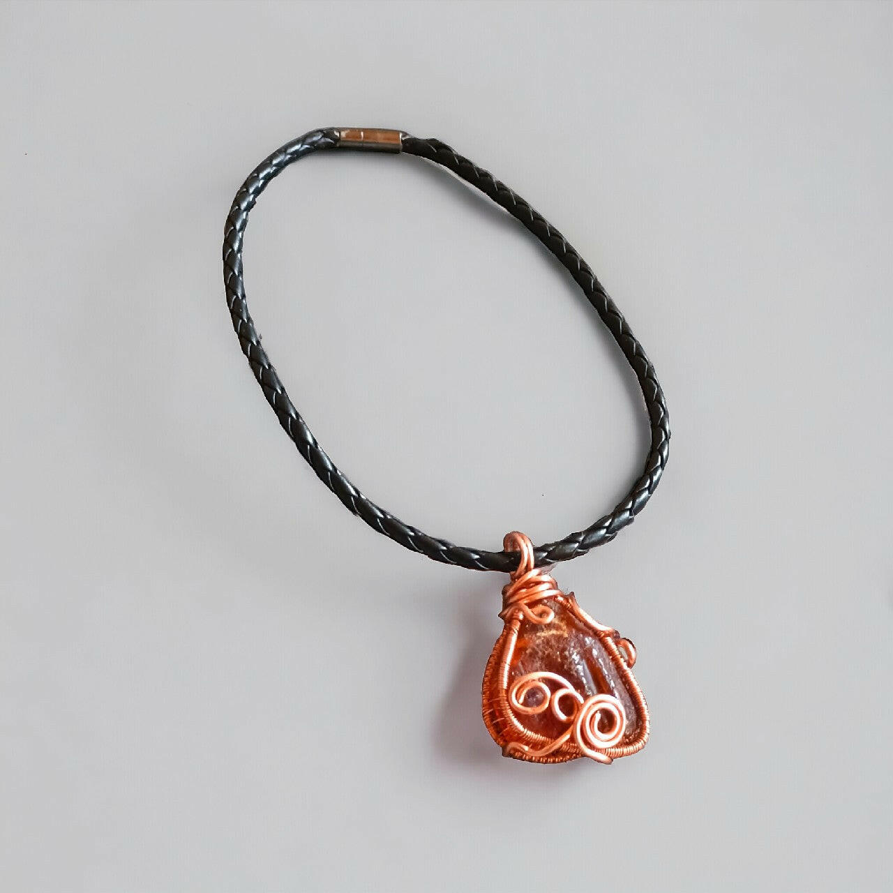 Wisiorek handmade łączący naturalne piękno surowej bryłki bursztynu bałtyckiego z ciepłym blaskiem miedzi w technice wire wrapping. Bursztyn o bogatej teksturze. Zawieszony na wygodnym, plecionym rzemieniu w kolorze czarnym, zapinany na magnes. Długość 42 cm.