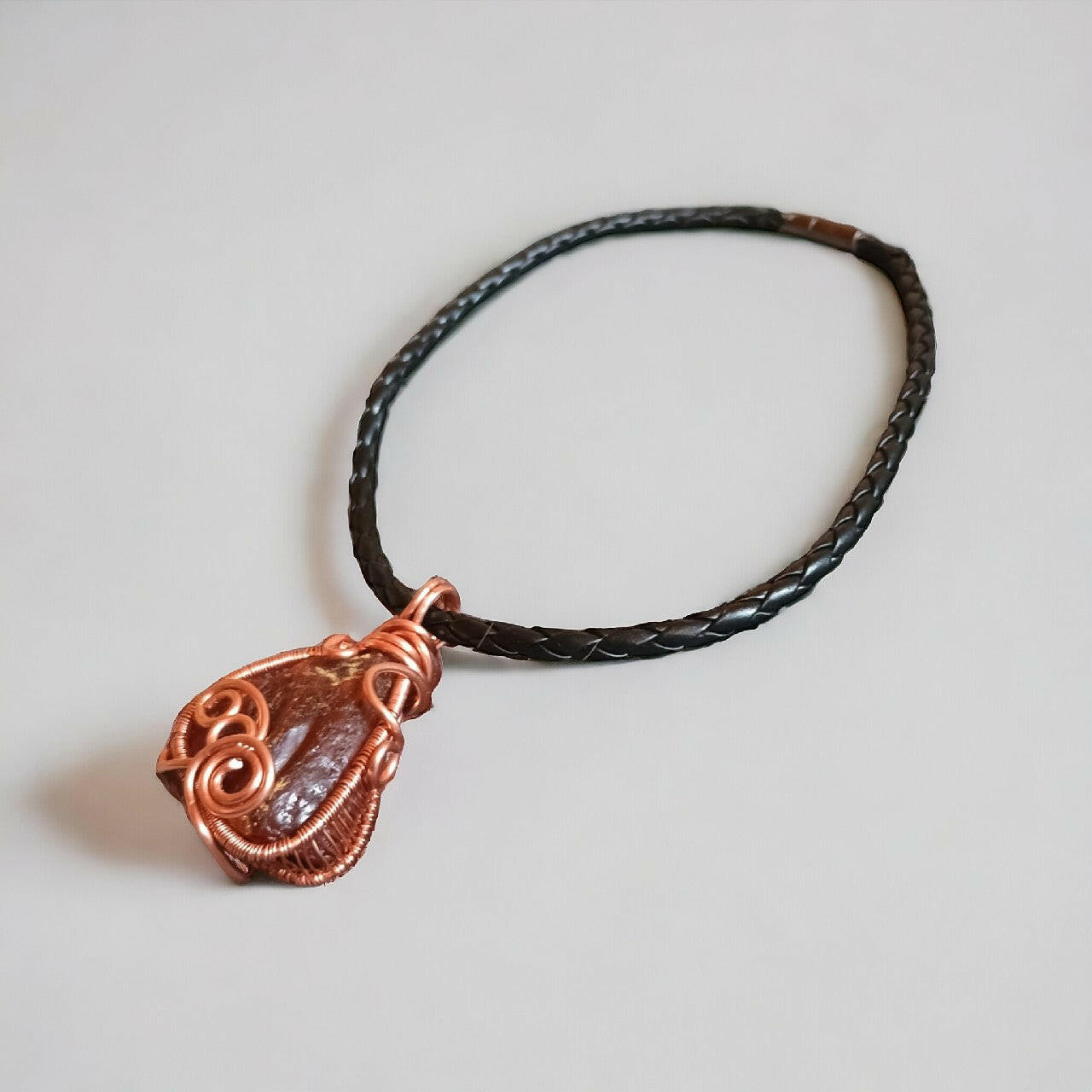 Unikatowy wisiorek z surowego, organicznego bursztynu bałtyckiego, ozdobnie owiniętego miedzianym drutem techniką wire wrapping. Bursztyn o charakterystycznej strukturze. Zawieszony na stylowym, plecionym rzemieniu z łatwym w użyciu zapięciem magnetycznym. Długość całkowita 42 cm.
