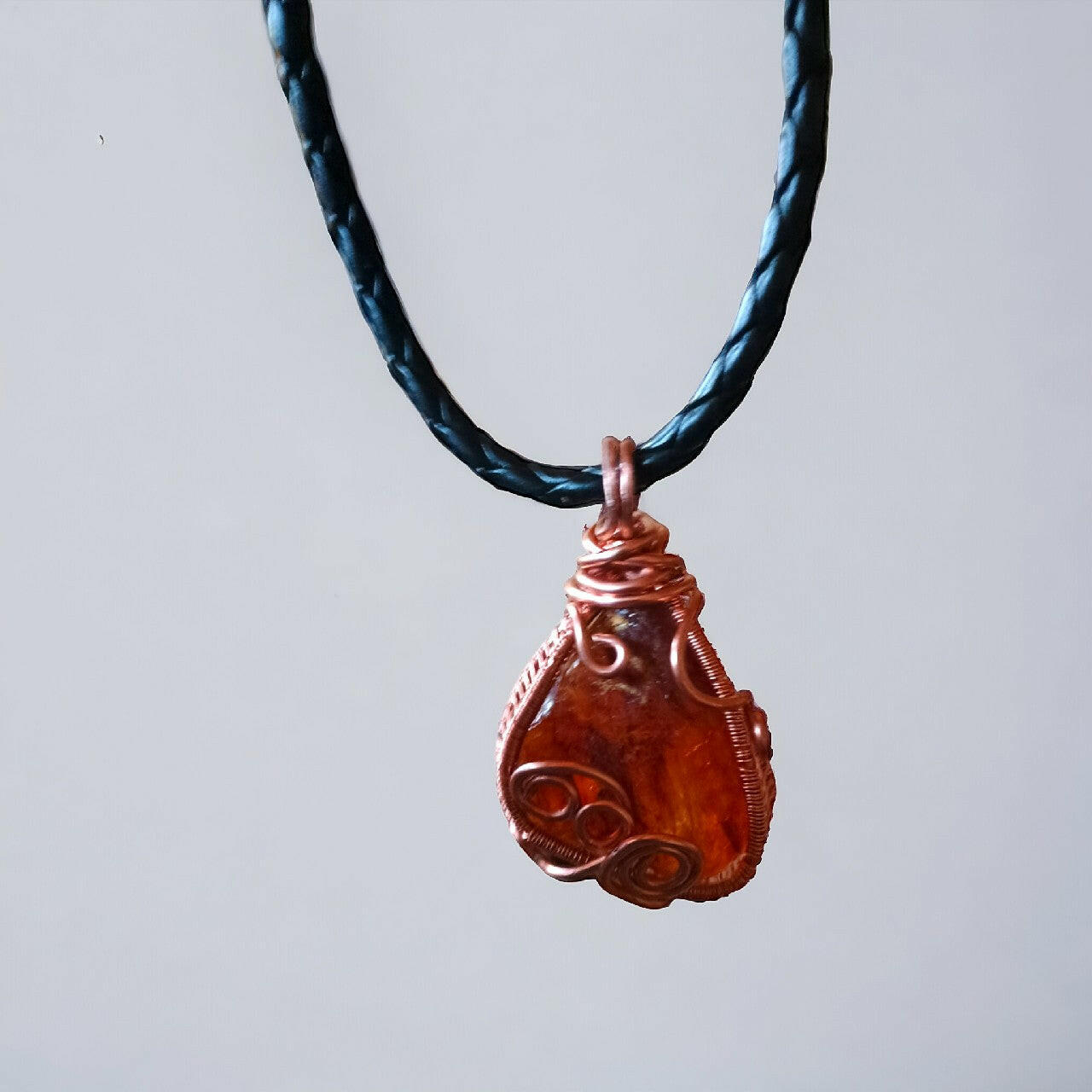 Wisiorek z surową bryłką bursztynu bałtyckiego o ciepłej, bursztynowej barwie, ręcznie opleciony miedzią techniką wire wrapping. Zawieszony na solidnym, czarnym, plecionym rzemieniu z bezpiecznym i wygodnym zapięciem magnetycznym. Długość 42 cm.