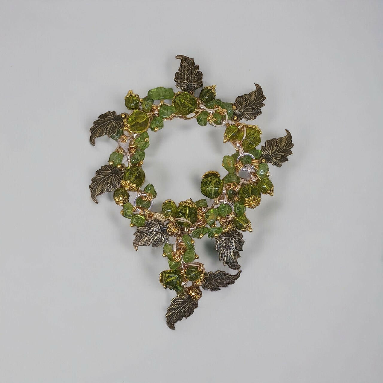 Unikatowa bransoletka z naturalnych peridotów o różnorodnych odcieniach zieleni, opleciona metalowymi listkami w kolorze starego brązu. Dodatki ze stali chirurgicznej nadają nowoczesnego akcentu, a regulowane zapięcie zwiększa jej funkcjonalność.
