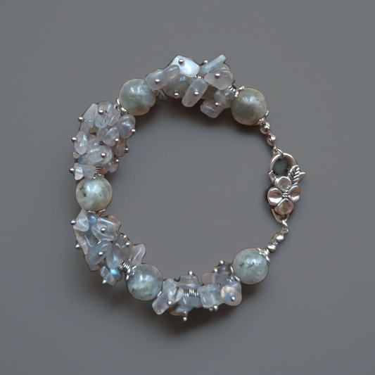 Subtelna bransoletka handmade z polerowanych labradorytów najwyższej klasy, mieniących się odcieniami szarości, błękitu i złota. Urozmaicona metalowymi elementami. Wyposażona w solidne zapięcie w formie kwiatka. Długość 19 cm.