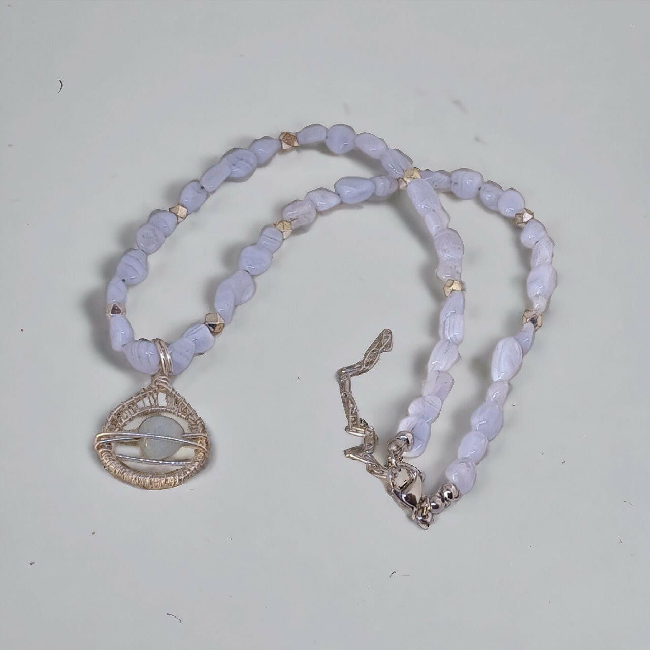 Delikatny naszyjnik handmade z nieregularnych, jasnoniebieskich chalcedonów. Srebrna, artystyczna zawieszka otacza subtelny, polerowany chalcedon. Wykończony srebrnym zapięciem i łańcuszkiem przedłużającym.