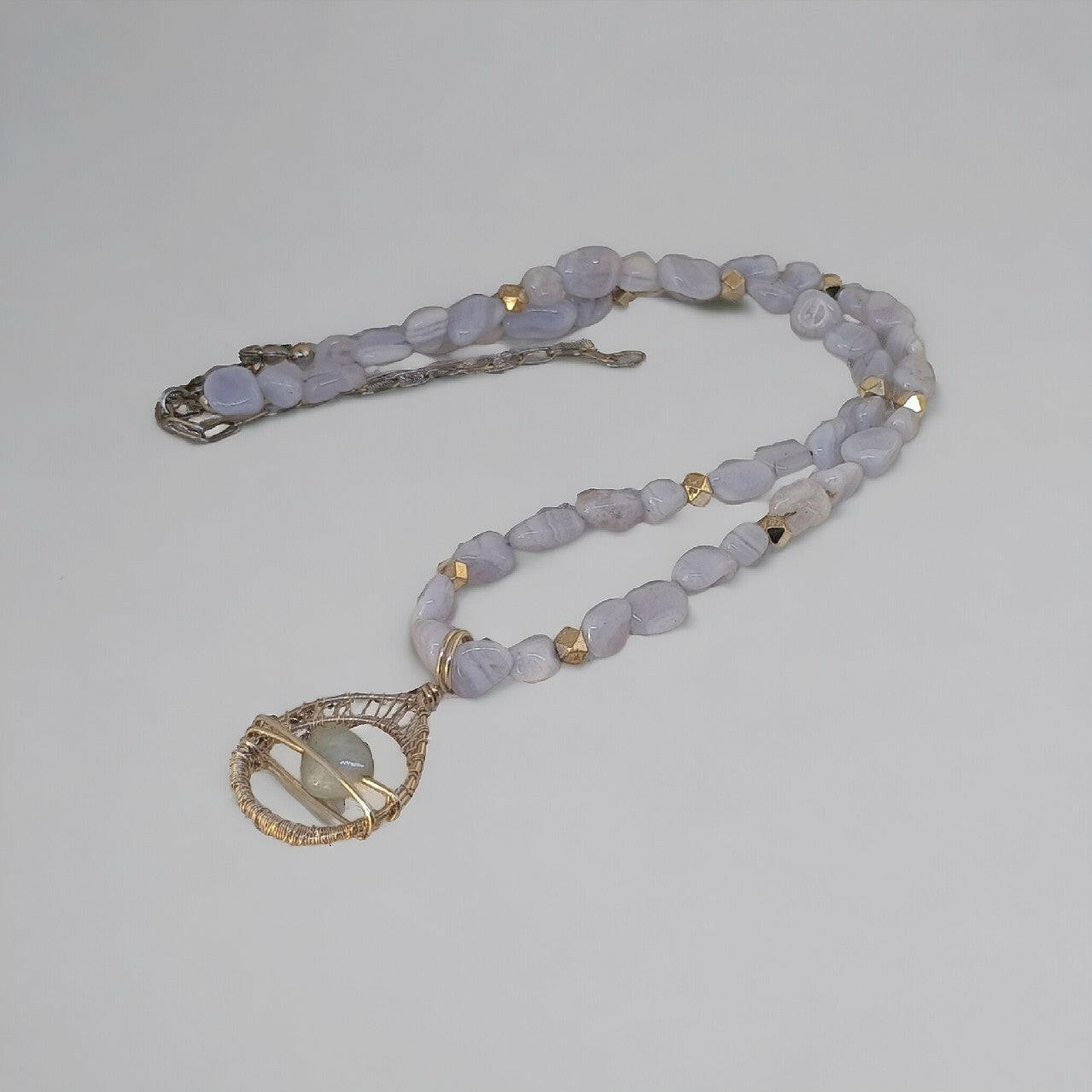 Ręcznie pleciony naszyjnik z drobnych, nieoszlifowanych chalcedonów w pastelowym odcieniu niebieskiego. Srebrna, ażurowa zawieszka z centralnie umieszczonym, gładkim chalcedonem. Srebrne zapięcie z możliwością regulacji dzięki łańcuszkowi
