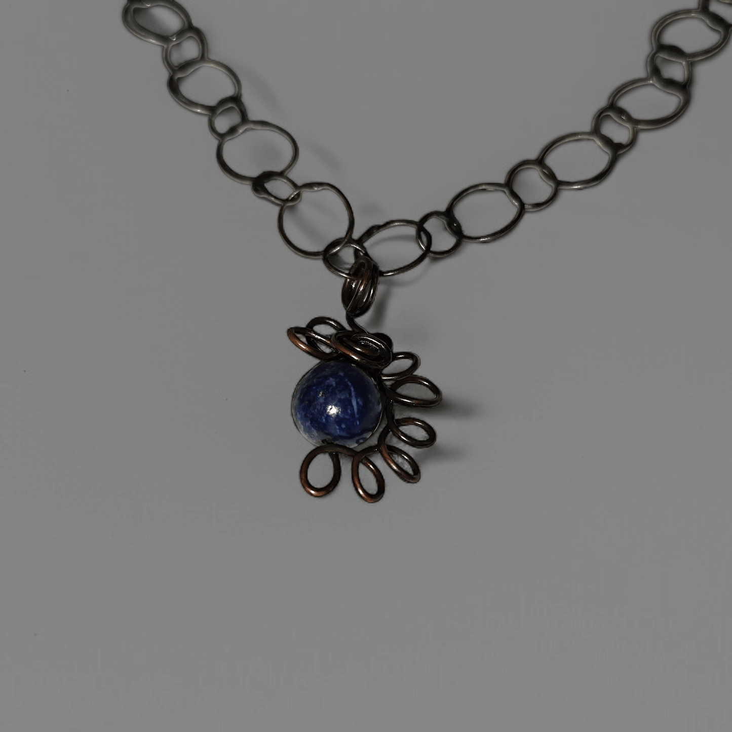 Mały wisiorek z lapis lazuli opleciony okręgami miedzi na ozdobnym łańcuszku z miedzi.Całość z efektem patyny