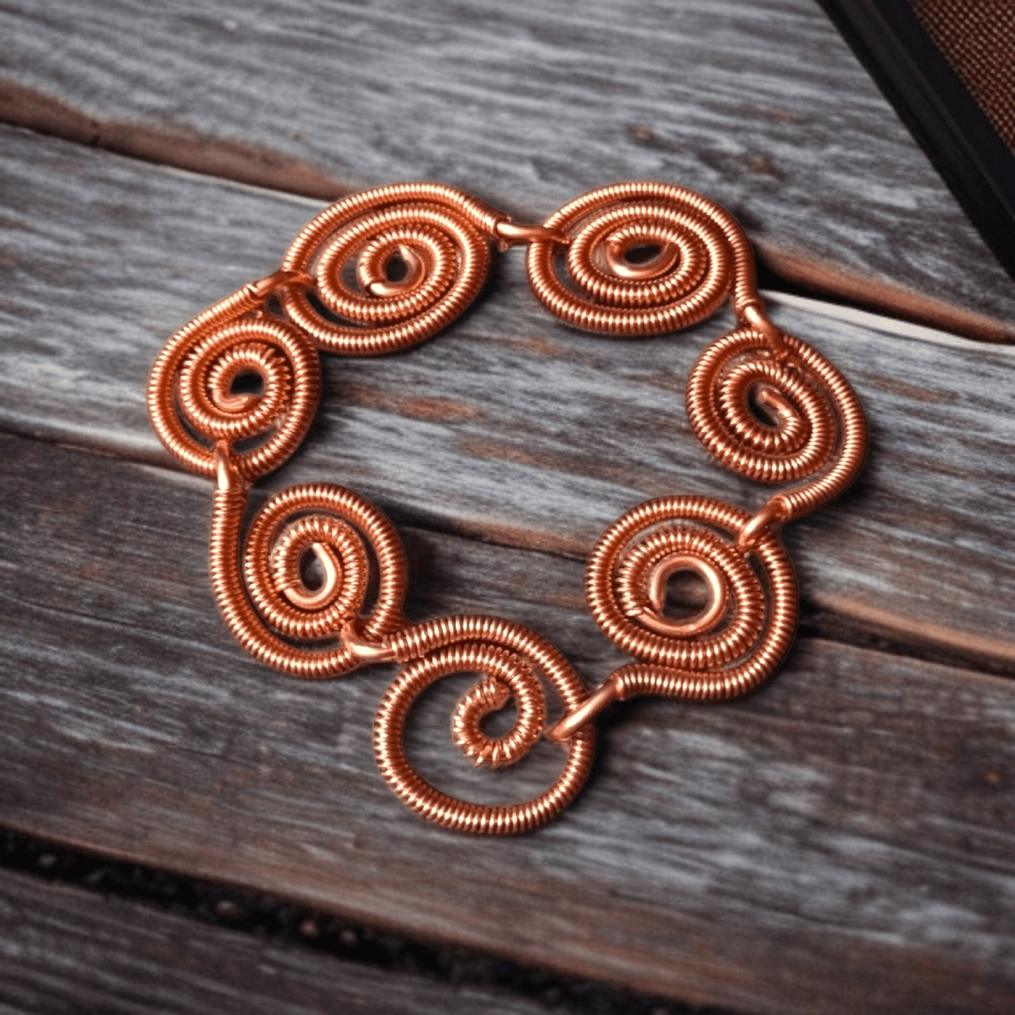 Bransoletka handmade z czystej miedzi składająca się ze spiralnych okręgów ozdobnie owiniętych i połączonych ze sobą i haczykowatym zapięciem