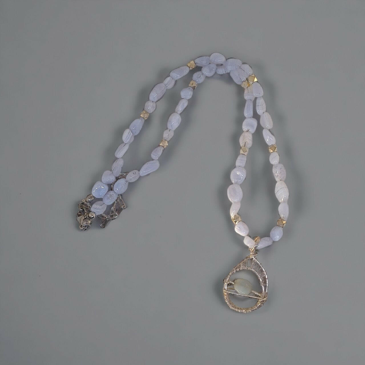 Subtelny naszyjnik z drobnych, matowych niebieskich chalcedonów. Ozdobna, srebrna oprawa wire-wrapping otacza jasny chalcedon w zawieszce. Srebrne zapięcie typu karabinek z łańcuszkiem do dopasowania długości