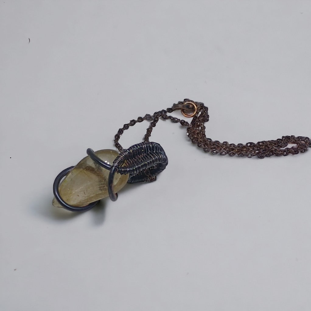 Wisiorek z kwarcu rutylowego i miedzi, wykonany metodą wire wrapping i pokryty patyną. Widoczna struktura oplotu z miedzianego drutu i inkluzje rutylu w kwarcu