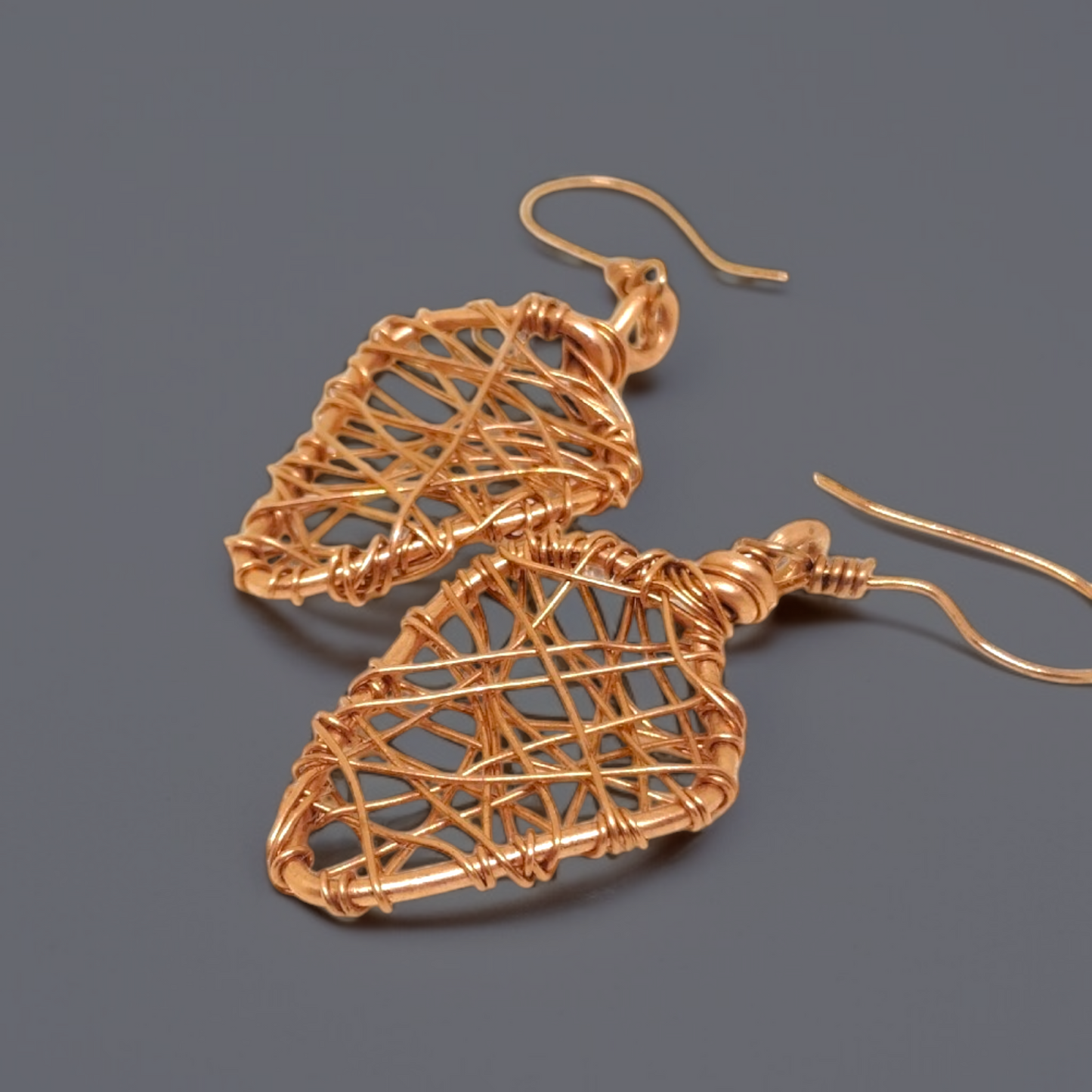 Kolczyki wiszące w kształcie średnich liści wykonane metodą wire wrapping na biglu z czystej miedzi.