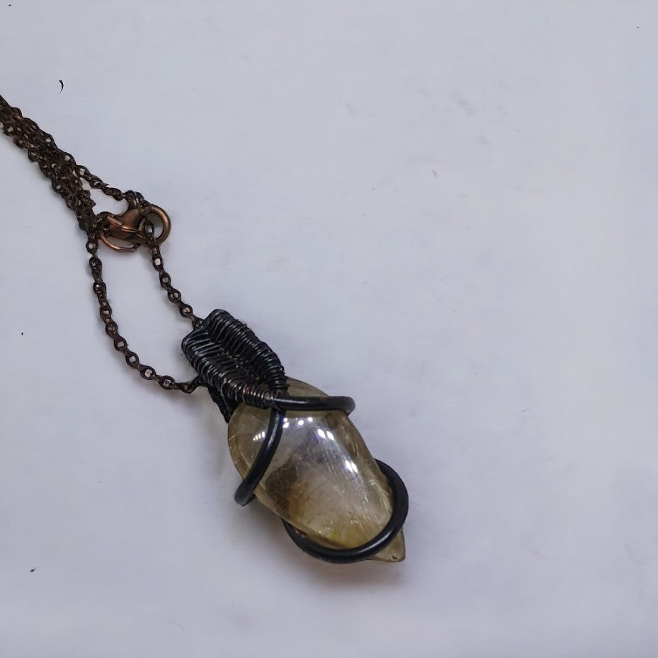 Detal wisiorka wykonanego ręcznie z kwarcu rutylowego i miedzi. Technika wire wrapping z oksydowaną miedzią tworzy niepowtarzalny i stylowy dodatek